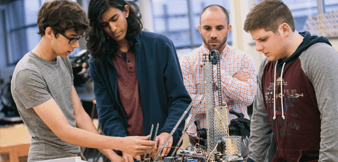 A teacher with 3 students in a classroom building a robot