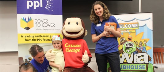 Curious George posing with a student and PPL volunteer