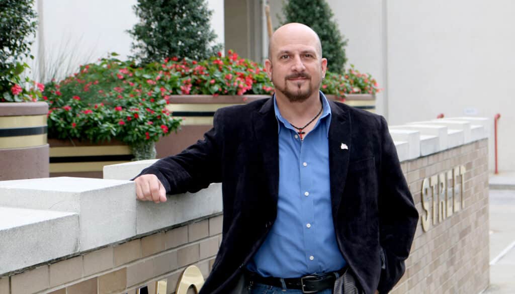 A man in a navy blue jacket and blue shirt leans against a ledge outside the PPL building.