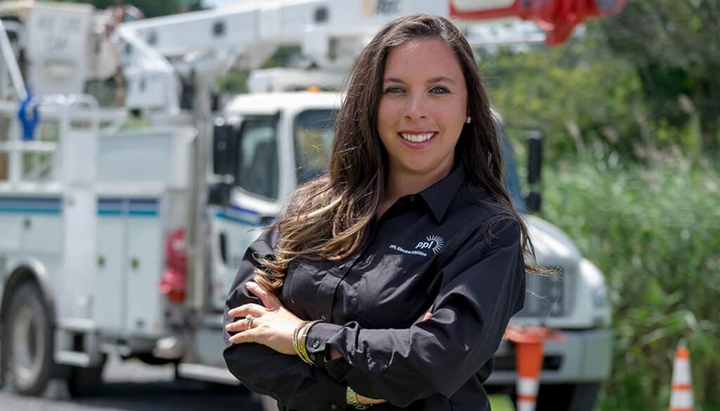 A woman with arms crossed stands in front of a PPL bucket truck