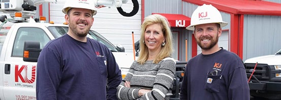 Two men with navy shirts and hard hat, pictured with blonde woman in striped sweater.