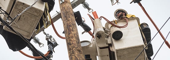 Lineworker atop a telephone pole, working from a bucket truck.