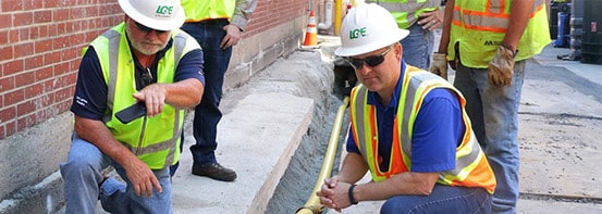 Men in fluorescant orange and yellow gear pose next to gas line.