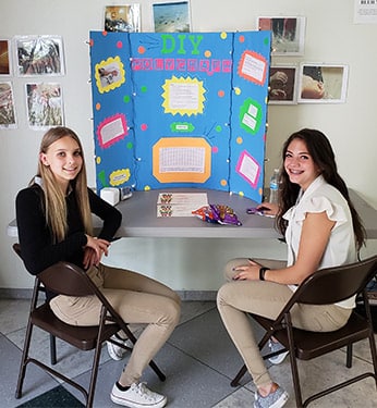 Girls sitting with their colorful poster boards at the STEM fair