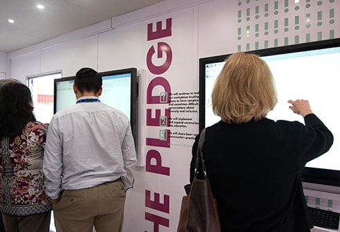 back of blonde woman wearing black sweater taking quiz on large tv screen