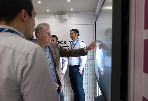 Man with white hair in tan suit pressing button on a large screen