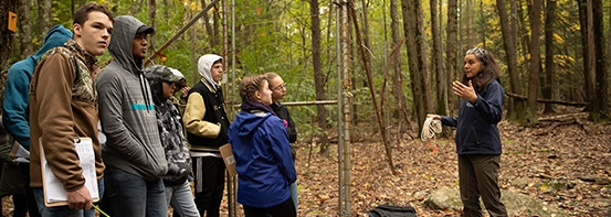 Dark haired woman explaining ecology program to group of teenagers in the woods