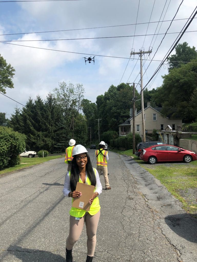 Female engineer with a clipboard oversees drone operators and drone near electric lines.