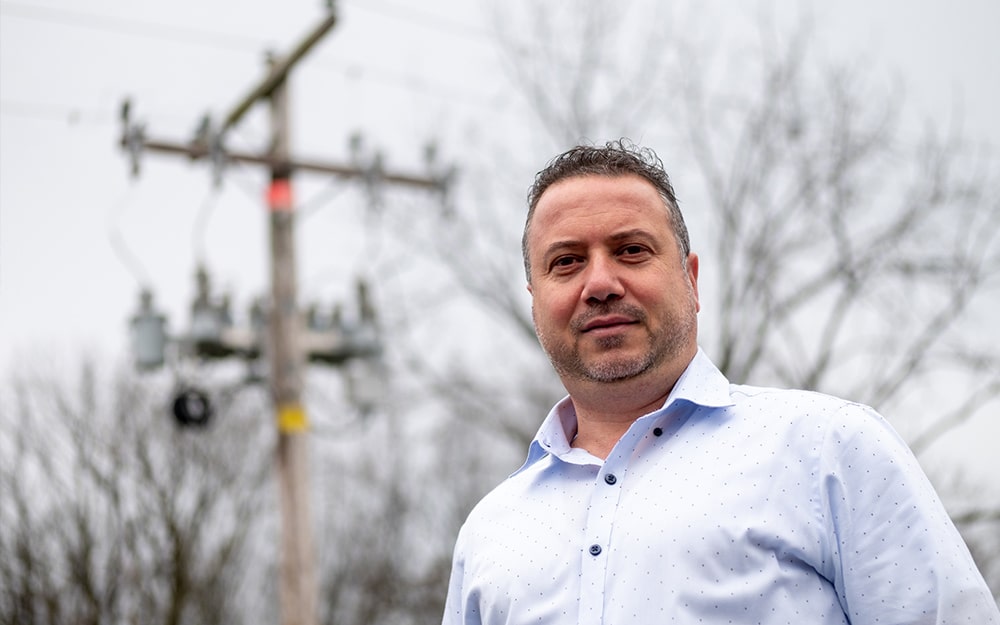 Photo of engineer Bashar Jarrah stands in front of electric distribution lines.