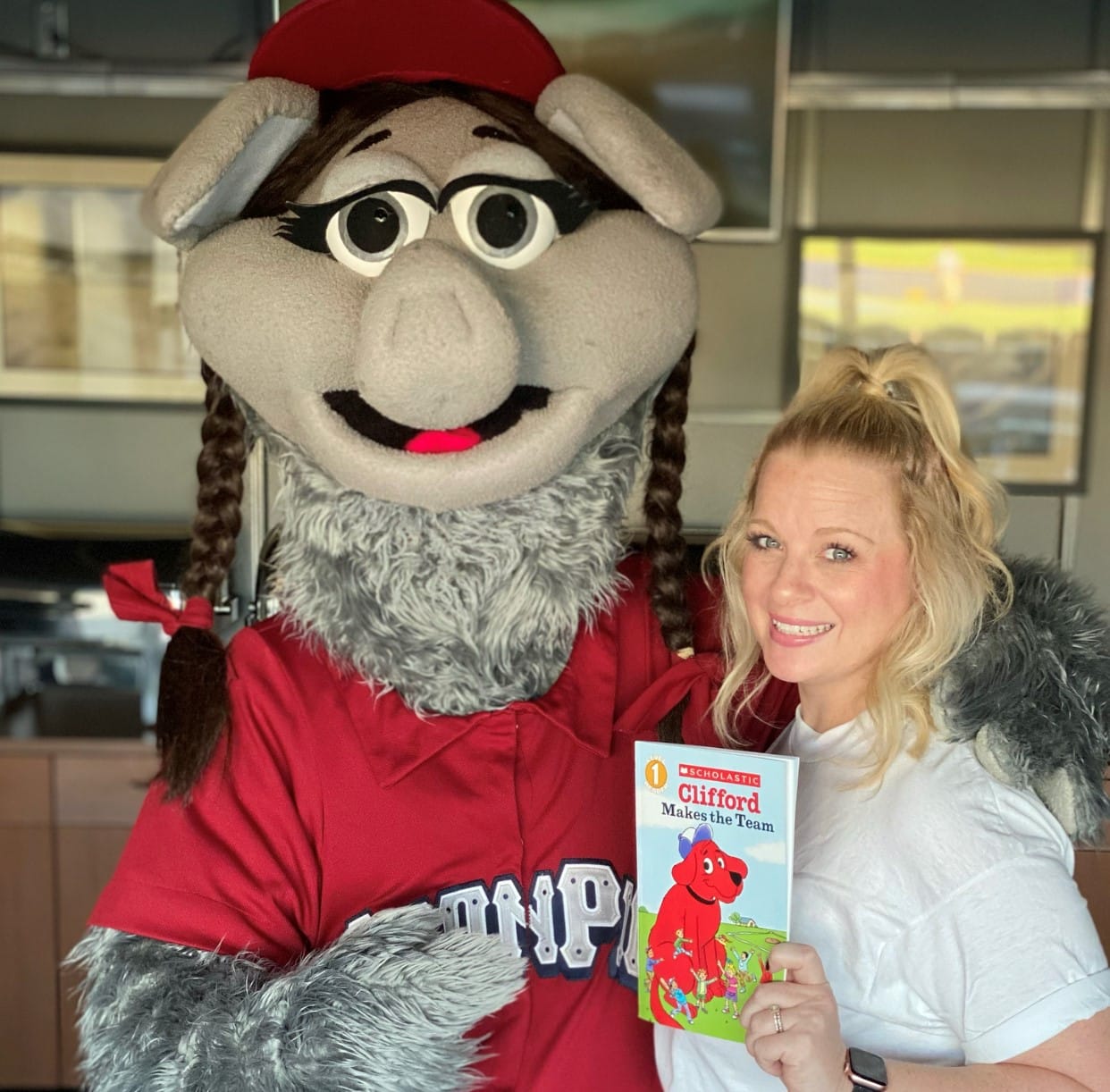 Kathleen Oswalt and FeFe the mascot of Lehigh Valley Iron Pigs posing with a book they read for children virtually