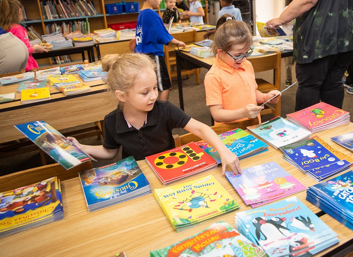 Little girl picking up a book on a table full of children's books