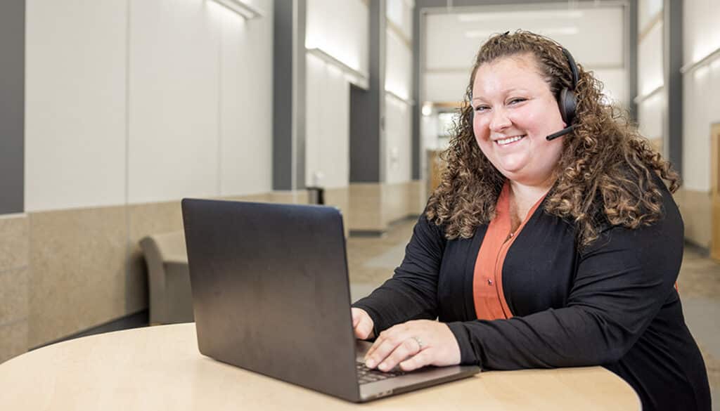 A customer service employee sits in front of her laptop smiling.